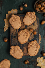 Acorn-shaped shortbread cookies on an aged wooden board. Oak leaves and acorns in the background. Autumn baking. Top view