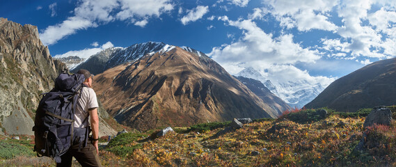 Panoramic view of tourist with backpack against picturesque mountain landscape during Annapurna Circuit trek in Himalayas, Nepal.