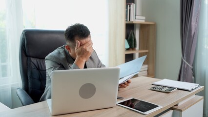 Thoughtful Asian Businessman working on laptop on Desk at office
