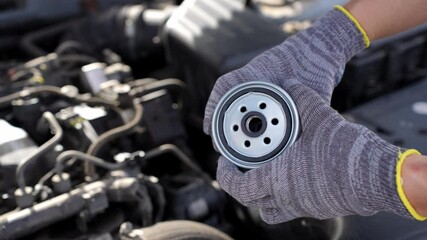 Auto mechanic is replacing fuel filter. Man holds diesel fuel filter in hands against engine compartment background, close-up. Auto parts replacement concept