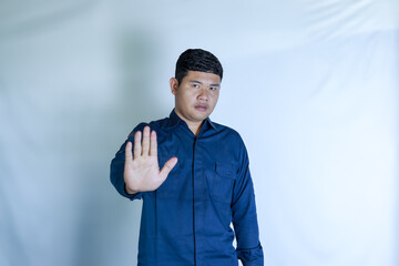 Young Asian man in blue shirt on white background gesturing to stop