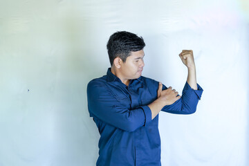 an asian man in blue shirt holding his hand on his bicep showing muscles on a white background