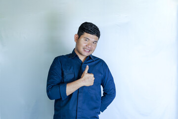 Excited Asian man wearing blue shirt giving thumbs up hand gesture as a sign of approval, isolated on white background