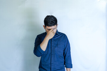 young asian man in blue shirt holding head with hands, his face showing pain expression, headache with white studio background. Concept of disease