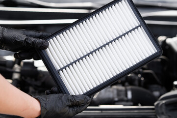 Auto repairman holding car air filter in hands , in front of car engine, examining it carefully,...
