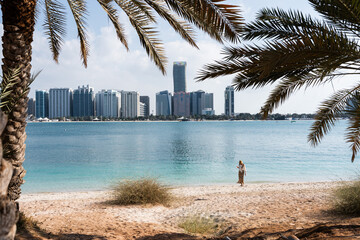 Tourist woman walking on the beach with city skyline in the background in abu dhabi