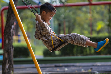 Little kindergarten asian boy enjoy play swing bar outdoor playground happy time