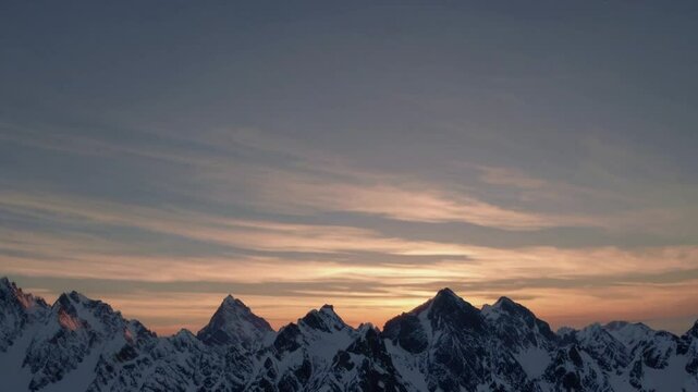  Silhouettes of snow-covered mountains against a colorful sunset with soft clouds in the sky, overlaid with an Adobe Stock watermark and video player interface elements