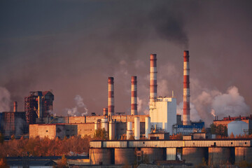 Metallurgical plant on the river bank in bright sunset light. Thick smoke is coming from the...
