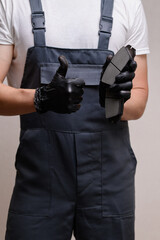 Auto mechanic in overalls holds two brake pads in hand, shows thumb up, close-up. Auto parts...