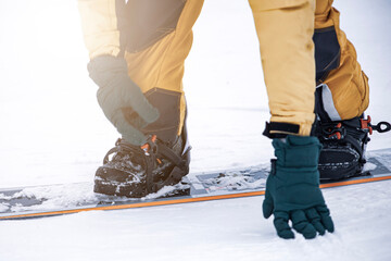 snowboarder on high mountain at ski resort preparing for freeride fastens strap on binding,...