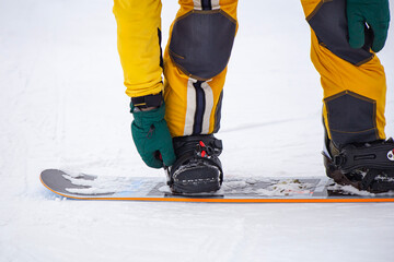 snowboarder on high mountain at ski resort preparing for freeride fastens strap on binding,...