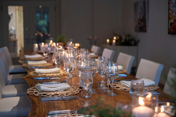 Untouched wooden dinner table served with glassware, silverware and candle decorations for gathering and celebration at a small cozy rustic winery restaurant, selective focus.