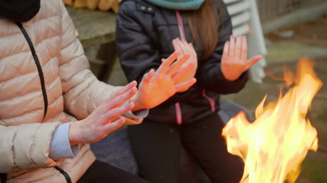 Sister and brother extending hands toward fire, feeling warmth from bright flames. Encouraging family moments Appreciating togetherness. Girl and boy sitting near burning wood, enjoying heat and