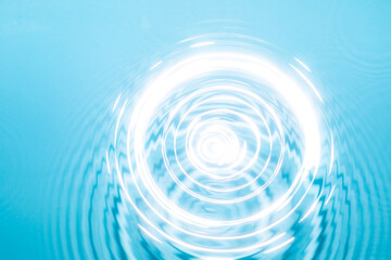 Circular ripples expanding in clear blue water under bright light at a tranquil location.