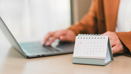Monthly calendar April 2025 on desk beside professional using laptop, illustrating schedule...