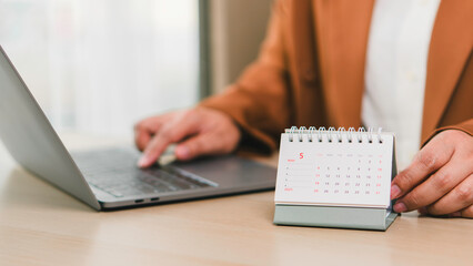 Monthly calendar May 2025 placed on office desk next to professional working with laptop, illustrating business schedule, daily planning, task management, deadlines, and productivity enhancement.