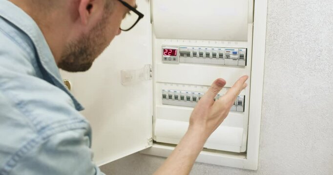 Man opens electrical circuit breaker panel switching on. Guy shows thumbs up gesture reflecting joy due to restoration of electricity supply in fuse box