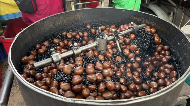 Roasting chest nuts with hot pebbles using a roaster at china town Malaysia.Chest nuts roasted Closeup slow motion.