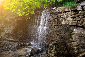 A picturesque waterfall surrounded by green foliage and rocks, glowing in sunlight. Ideal for nature lovers, peace, and scenic outdoor environments.