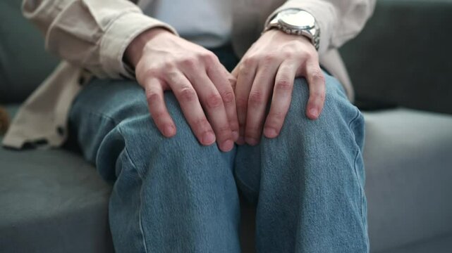 Legs shaking in a guy in blue jeans.
Uncontrollable leg shaking.
Severe stress in a guy.
A man is worried while sitting on a sofa.
Health problems