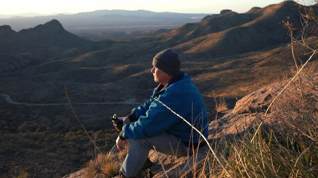 A man taking a break on a mountain summit, sipping water