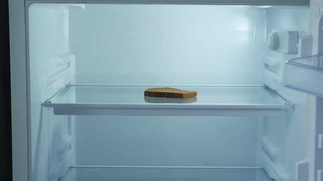 a piece of bread in an empty refrigerator is taken by a man's hand, the concept of food shortage, food crisis