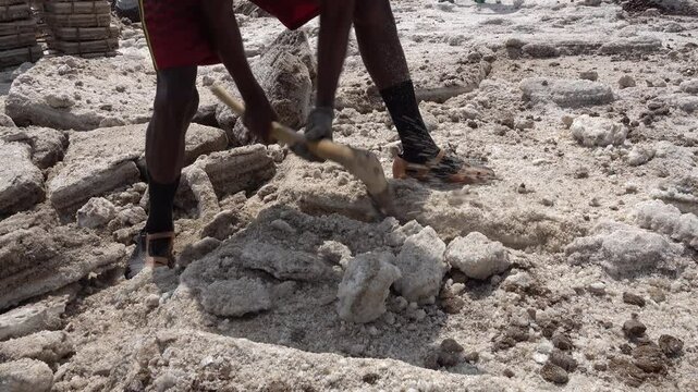 Salt mine worker uses large axe to chop blocks of salt in the Danakil desert, difficult working conditions in Ethiopia
