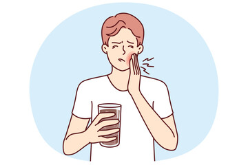 Man suffers from toothache caused by cold drink and needs pain medication and dentist. Guy with toothache associated with caries or stomatitis holds glass of medicine for mouthwash.