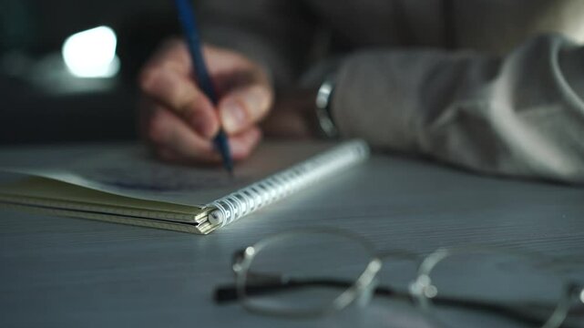 A man writes a script in a notebook with a pen.
A man at a desk writes in a notebook.
A copywriter writes in a notebook with a pen while sitting in an office