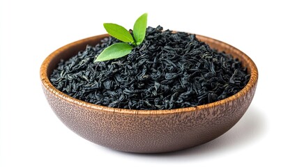 Black tea leaves in a wooden bowl with a green leaf on a white background,