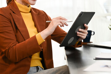 A woman in a yellow sweater is using a tablet with a stylus.