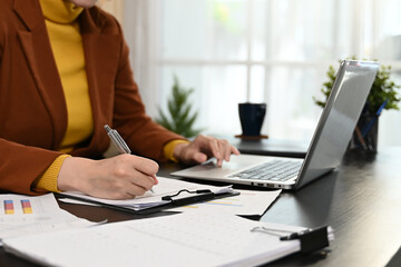 A woman is sitting at a desk with a notebook and pen. She is writing something down and she is focused on her work.