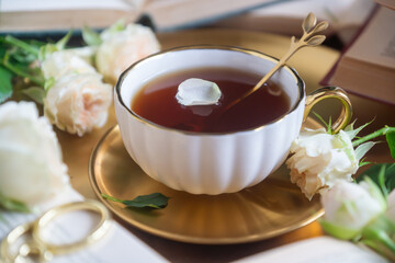 A cup of aromatic tea, a book and a rose on the table.