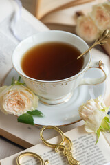 A cup of aromatic tea, a book and a rose on the table.
