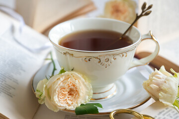 A cup of aromatic tea, a book and a rose on the table.