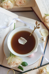 A cup of aromatic tea, a book and a rose on the table.