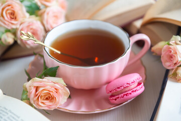 A cup of aromatic tea, a book and a rose on the table.
