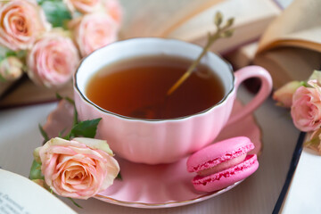 A cup of aromatic tea, a book and a rose on the table.