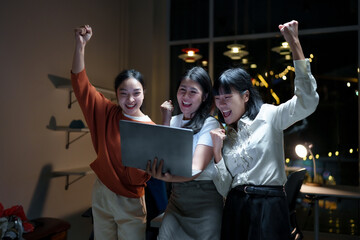 Jubilant businesswomen cheering, pointing at laptop screen, celebrating professional success in...
