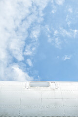 Blue sky frame the aircraft exterior of airplane fuselage with visible window and metallic texture.