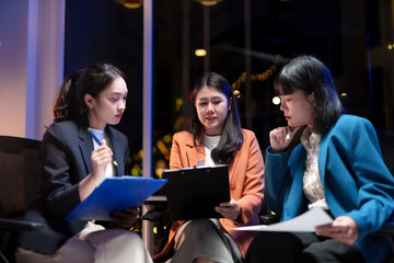 Group of asian businesswomen reviewing documents and having a discussion during a late night meeting at the office