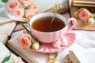 A cup of aromatic tea, a book and a rose on the table.