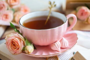 A cup of aromatic tea, a book and a rose on the table.