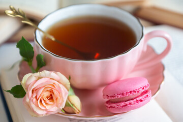 A cup of aromatic tea, a book and a rose on the table.