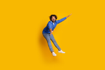 Obraz premium Cheerful young male jumping and gesturing dynamically against a vibrant yellow background showcasing joy