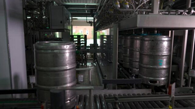 Metal beer kegs move along an automated conveyor system at a brewery for cleaning and filling. The high-tech production process ensures proper sanitization and preparation before beer is dispensed int