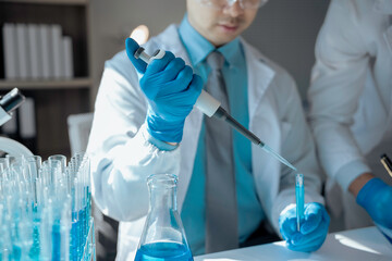 Scientist pipetting blue liquid into test tube, performing meticulous biological research with...