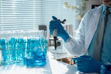 Scientist dripping blue liquid with a micropipette into a test tube in a laboratory with test tubes...