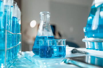 Blue filled scientific glassware conducting chemical research, pipette and tablet visible in soft focus laboratory setting